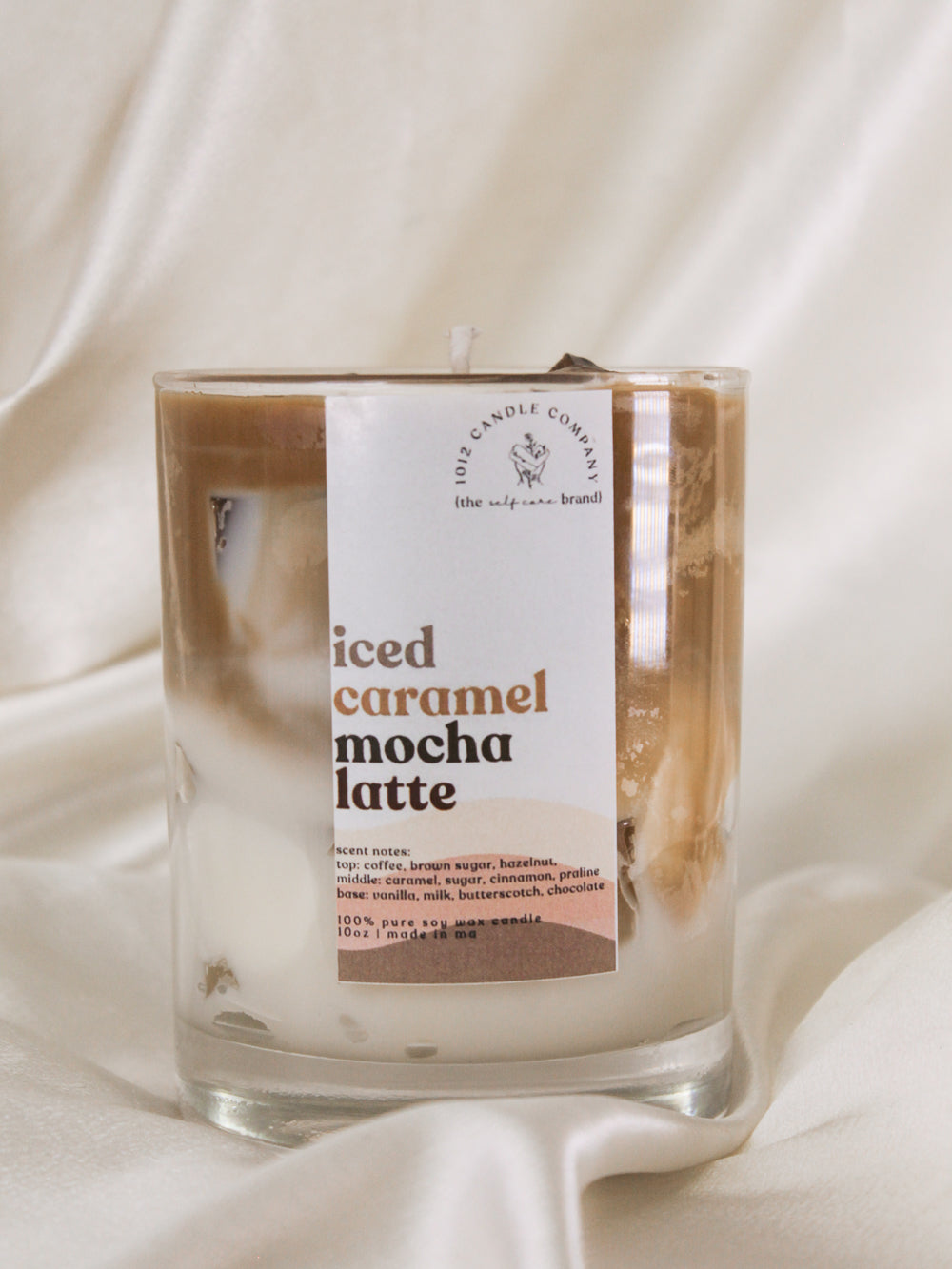 A candle in a clear jar that looks just like an iced latte with realistic layered look and ice cubes