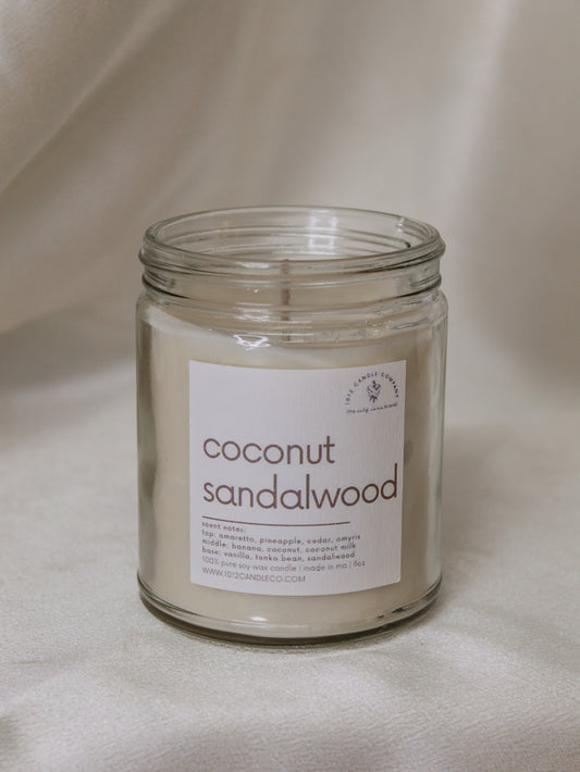 A soy wax candle in a clear jar labeled and scented like coconut sandalwood
