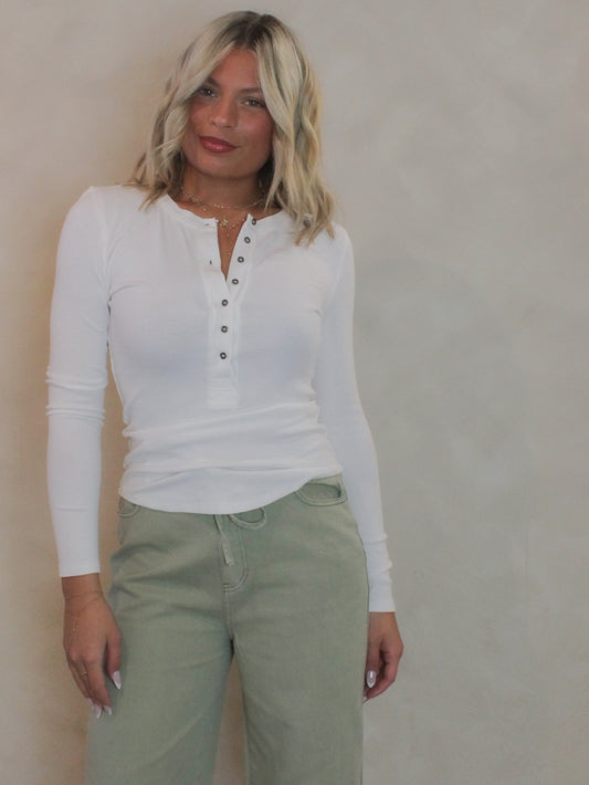 Woman wearing a white long sleeve henley top with sage green denim pants.