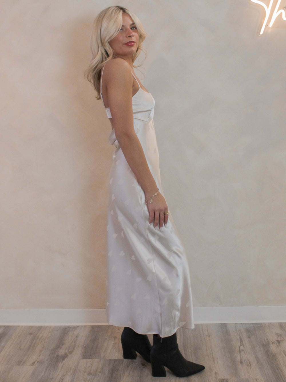 Girl wearing a satin, midi dress in a cream color with a subtle fun heart pattern