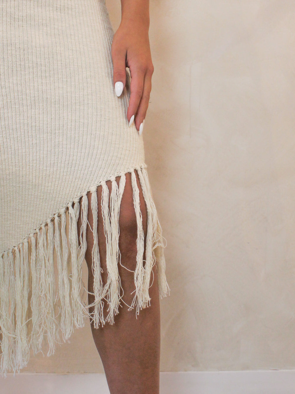 Detail view of a neutral knit dress with a fringe bottom