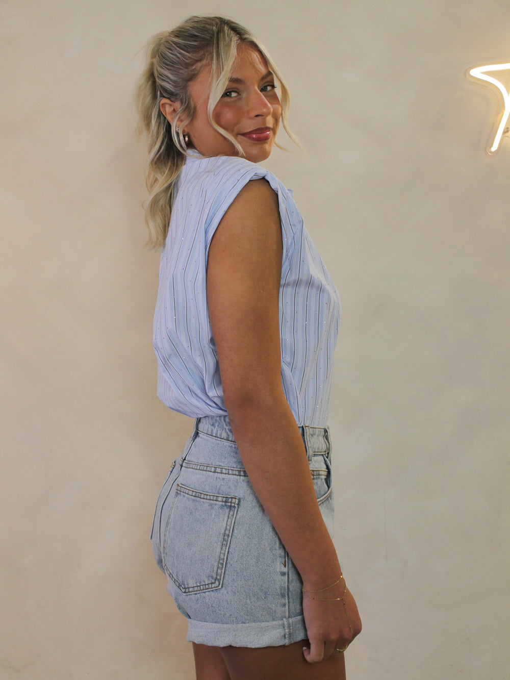 Woman wearing a sleeveless light blue button up tucked into denim shorts