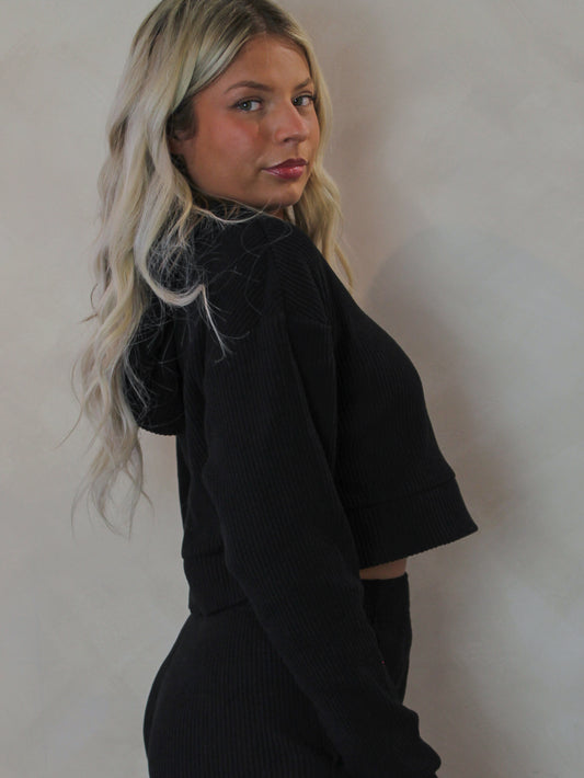 Model wearing a black cropped, long sleeve top with hood