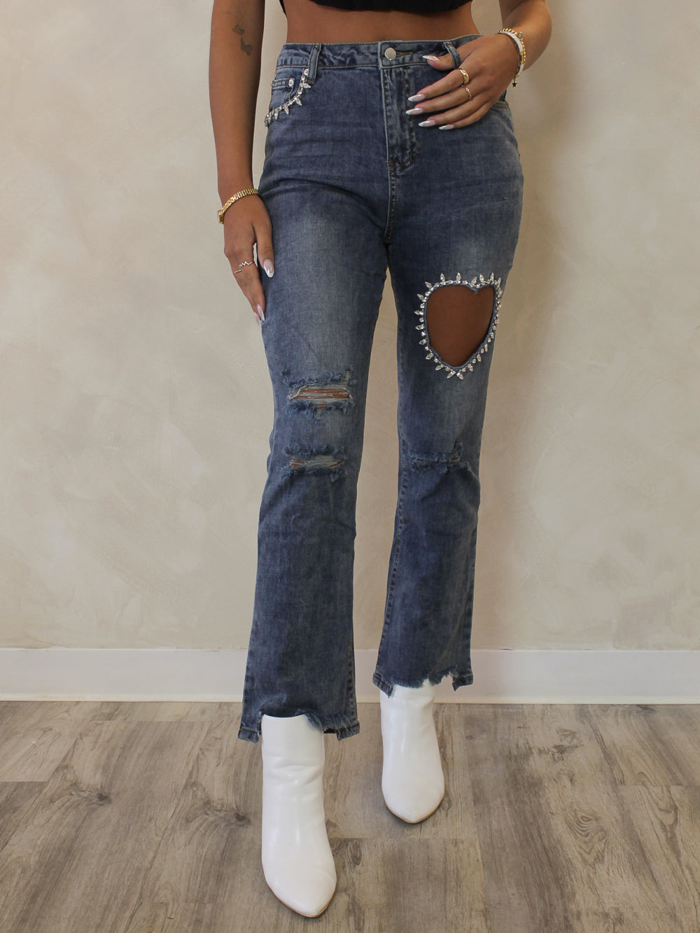 Woman wearing a pair of cropped, medium wash denim with cut out heart and rhinestone details