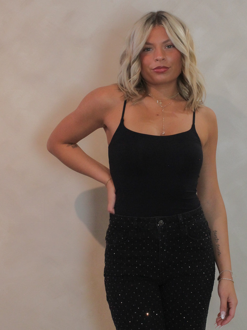 Woman wearing a black tank top and black pants with rhinestones.