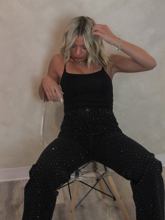 Woman wearing a black cami bodysuit with black rhinestone denim