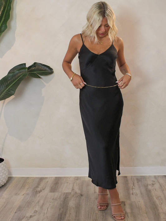 Woman wearing a black satin midi dress with subtle side slit