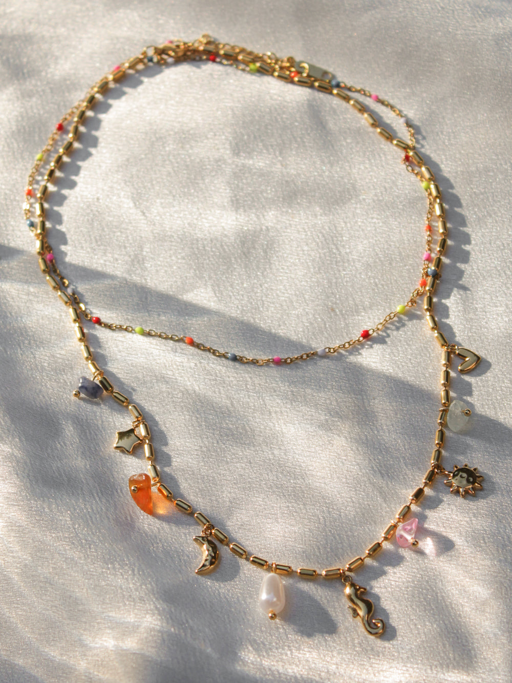 a double layered gold necklace with a colorful beaded layer and a layer with ocean and celestial charms