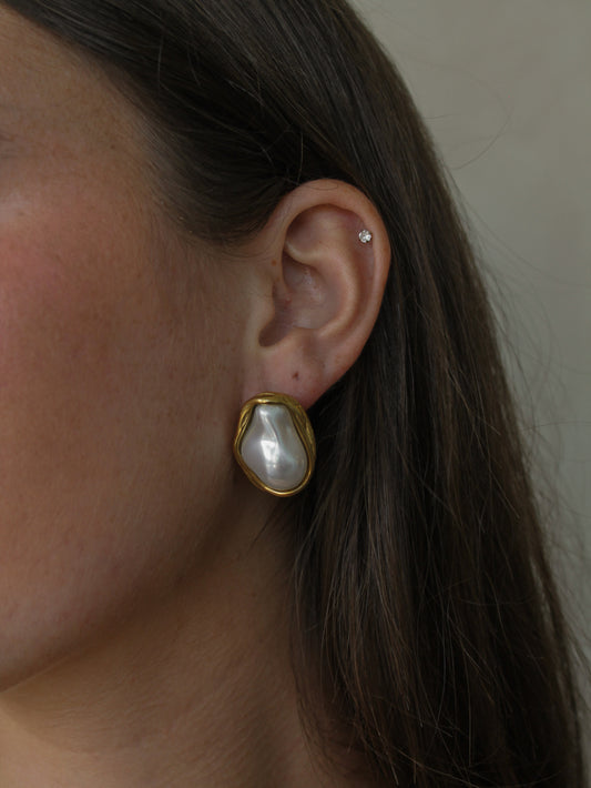 a girl wearing a gold oversized pearl earring with a gold outline