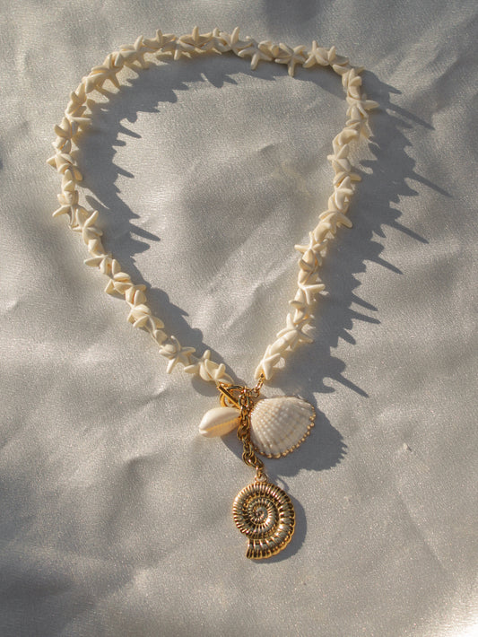 a necklace made of small star shell charms with a cluster of gold and seashell charms at the end
