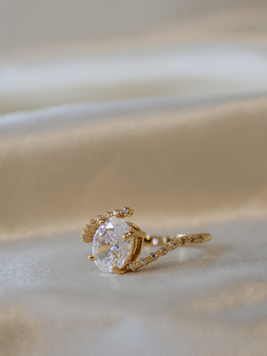 A gold ring with a large solitaire clear gemstone and small accent stones along the band.