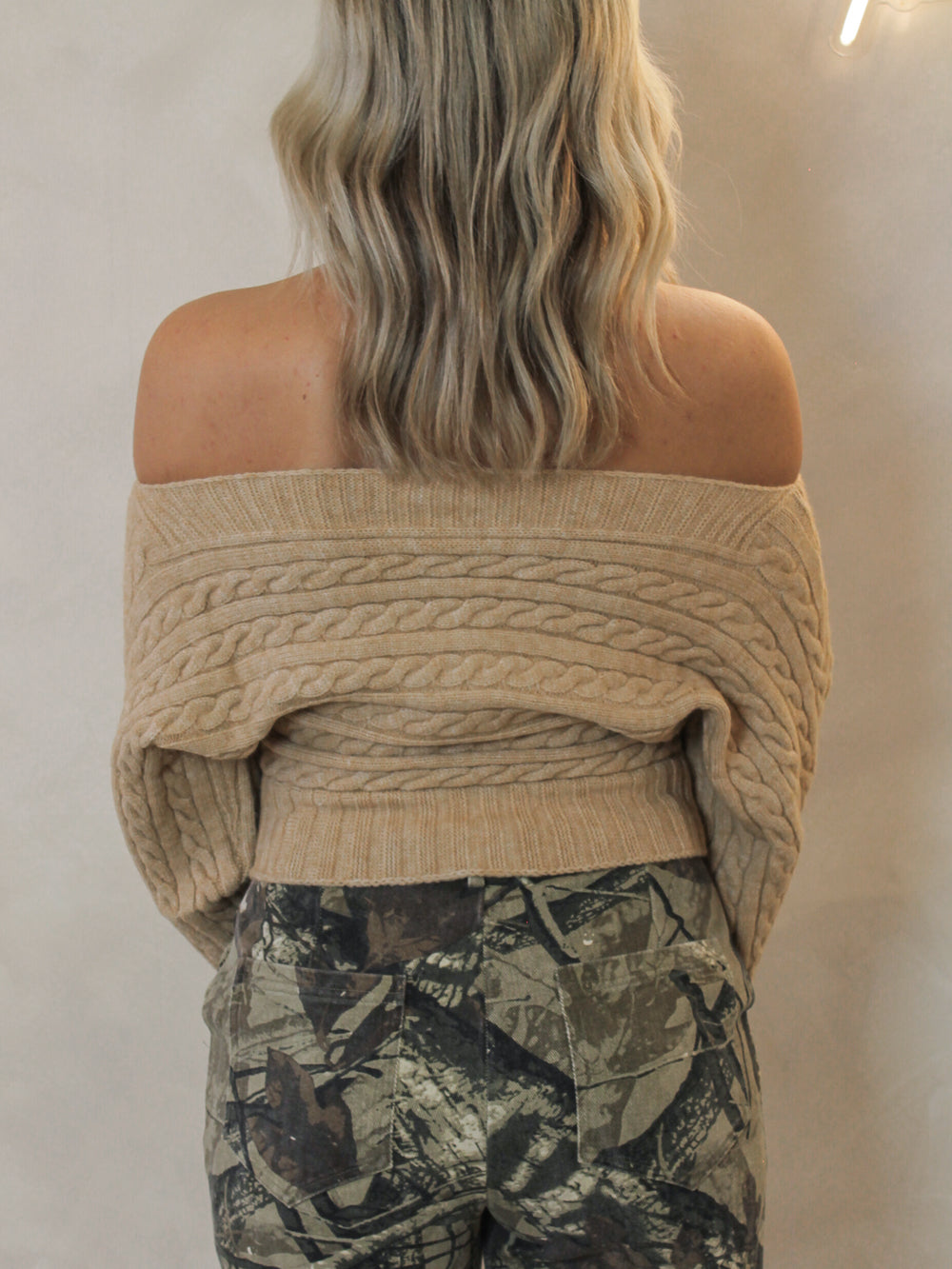 Woman wearing a beige off-shoulder sweater and camouflage pants against