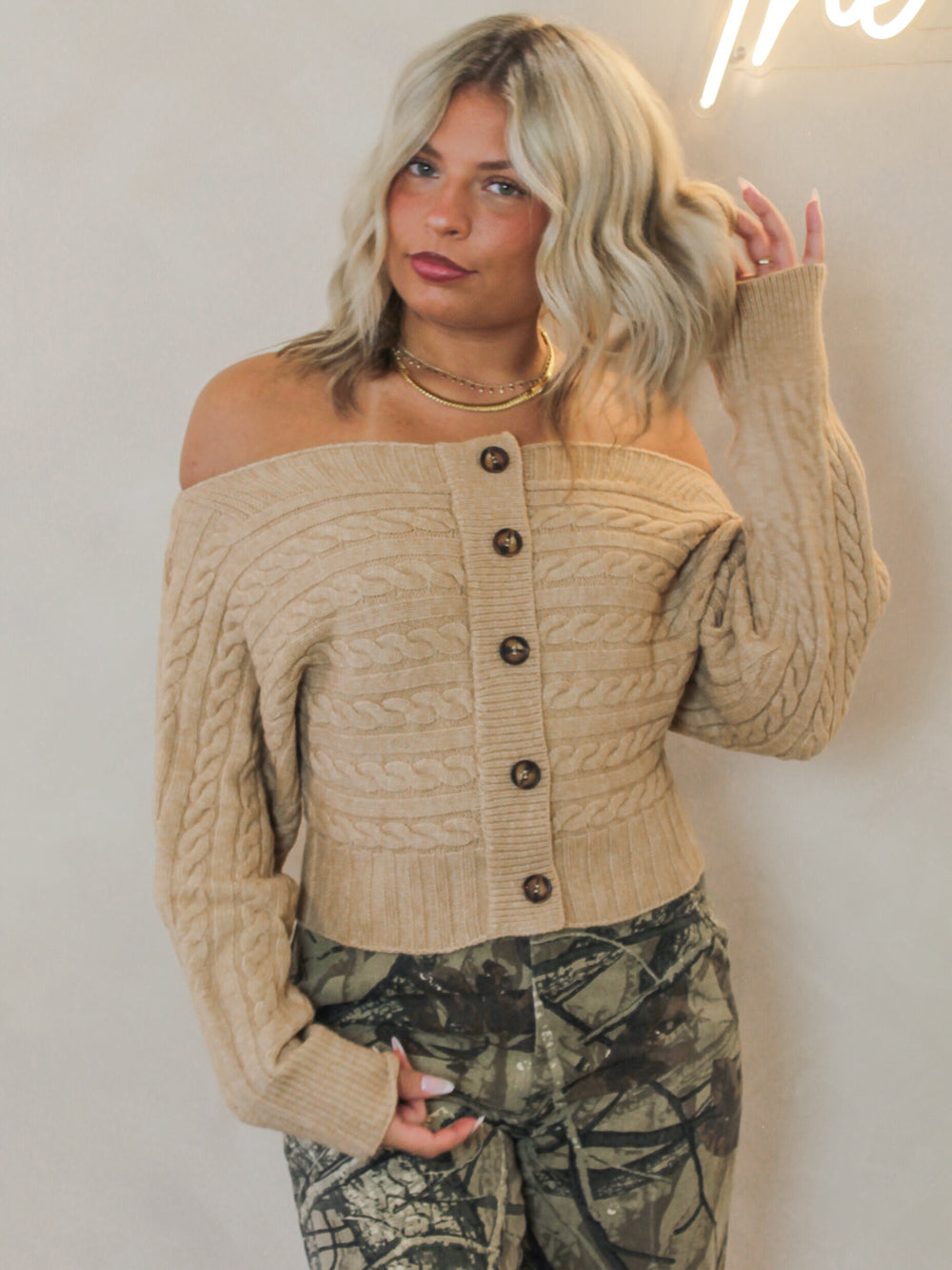 Woman wearing a beige off-shoulder cable knit cardigan with button details