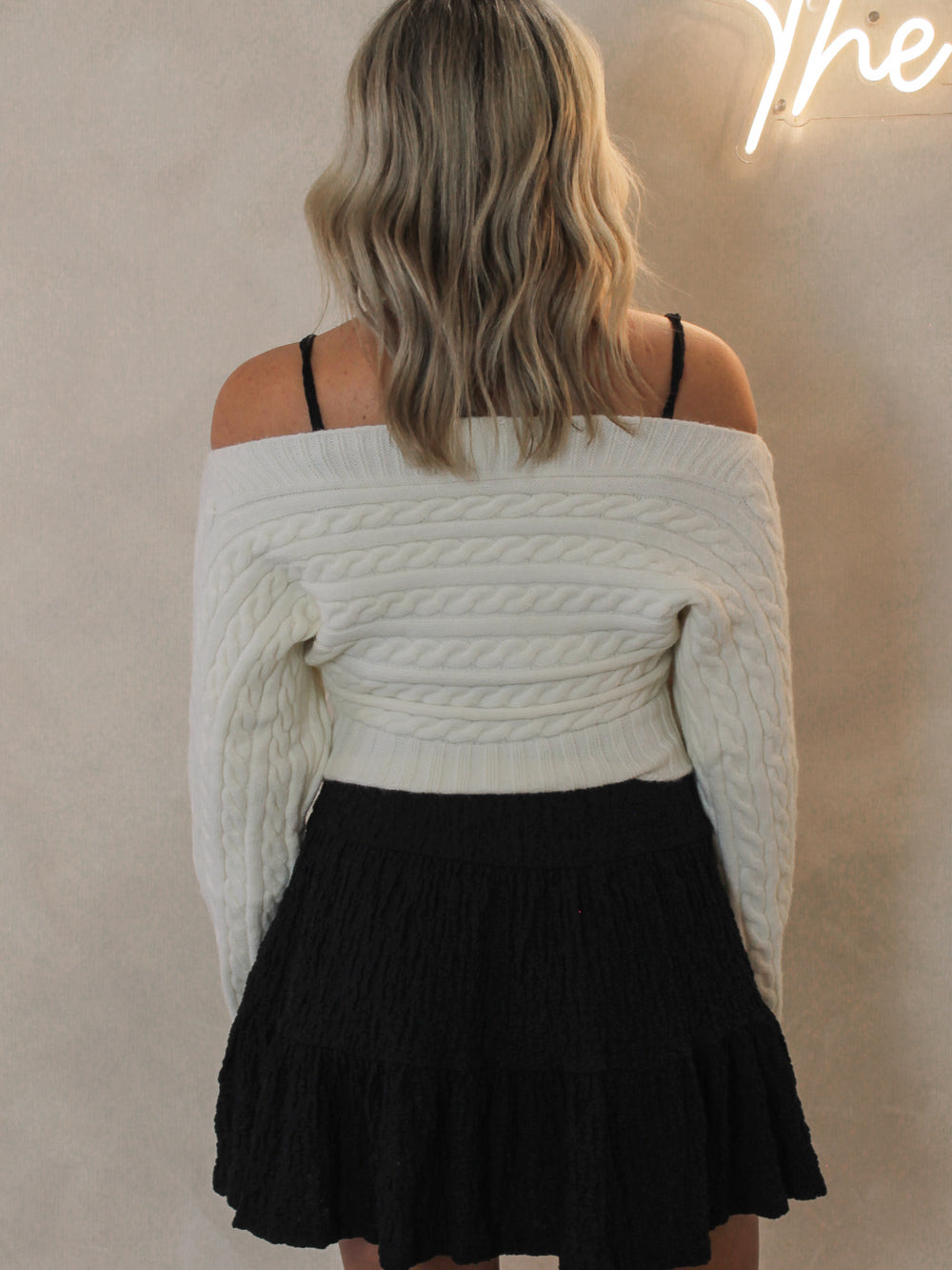 Woman wearing a cable knit off the shoulder sweater paired with a black mini dress