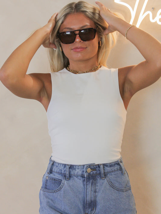 Women wearing a sleeveless, white, basic bodysuit with high neckline for layering and everyday wear