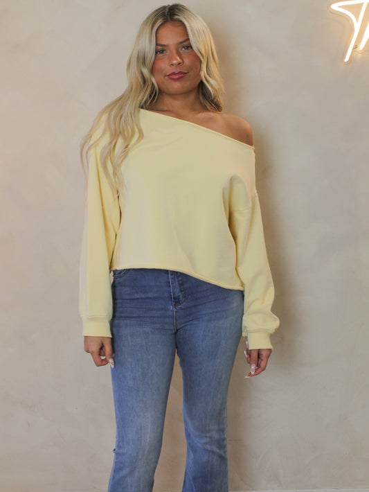 Model wearing a yellow off-shoulder sweater and blue jeans a
