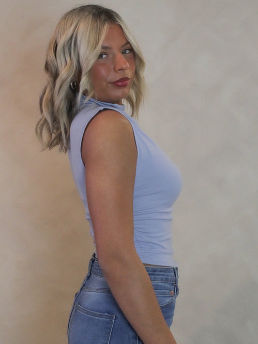 Woman wearing a baby blue top with a mocked neck and sleeveless silouette