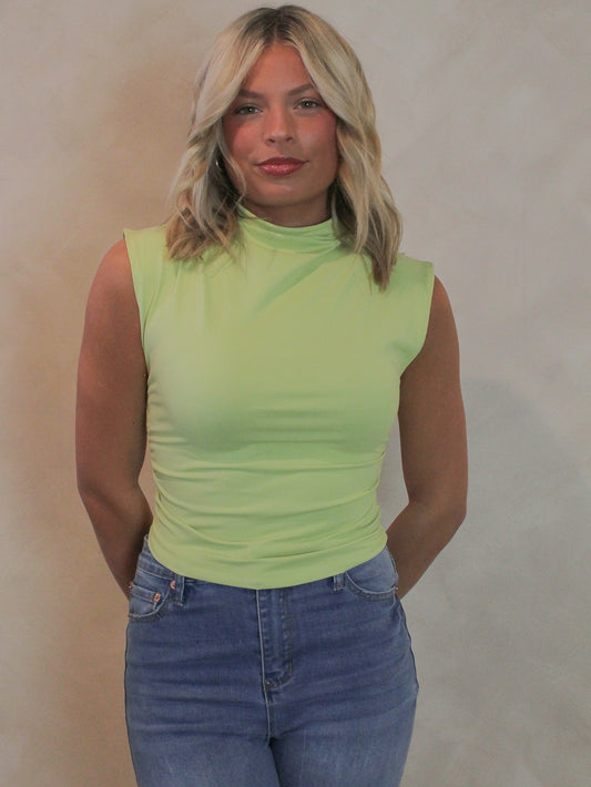 Woman wearing a lime green, mock neck sleeveless top