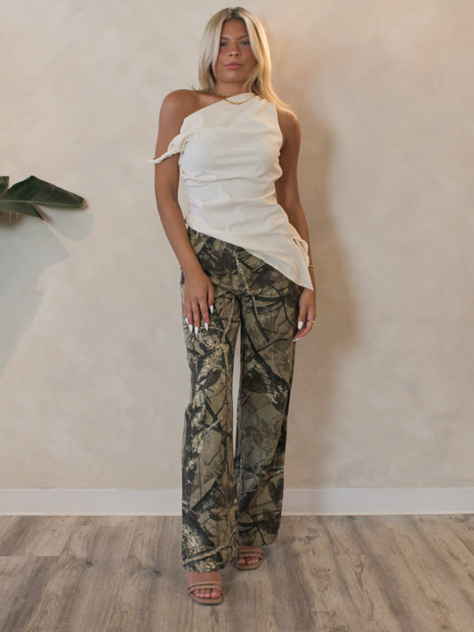 Woman wearing wooded camo pants styled with an asymmetrical cream top for a casual, street style outfit