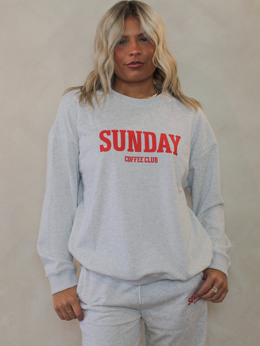 Woman wearing a grey crew neck sweatshirt with the words 'sunday coffee club'