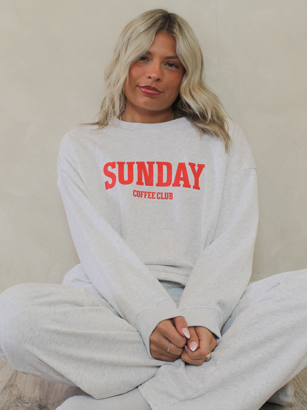Woman wearing a grey crew neck sweatshirt with the words 'sunday coffee club'