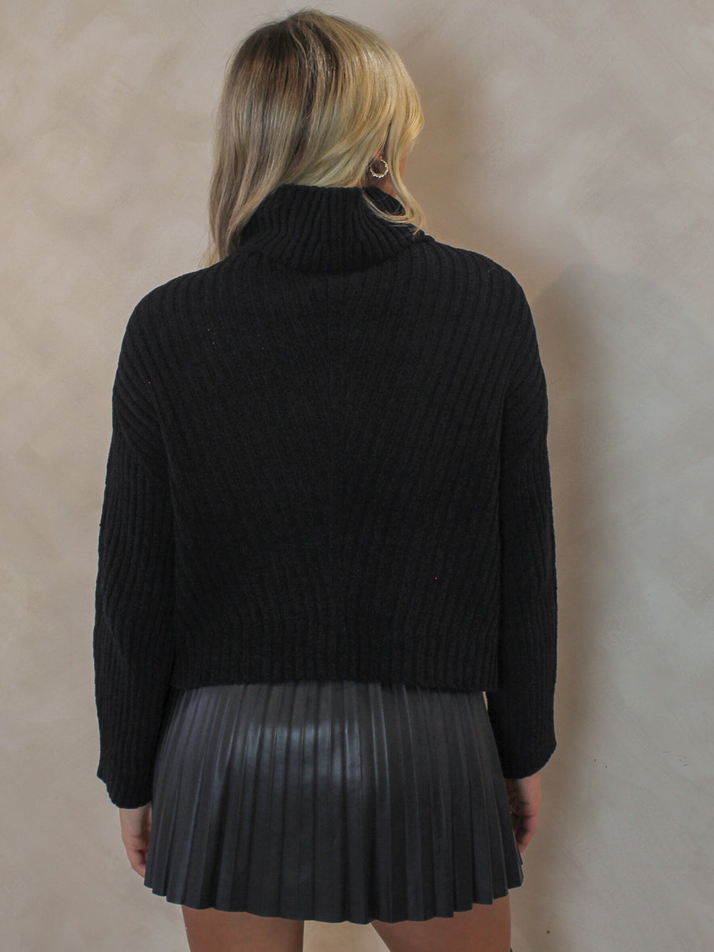 Woman wearing a black knit sweater with black pleated skirt