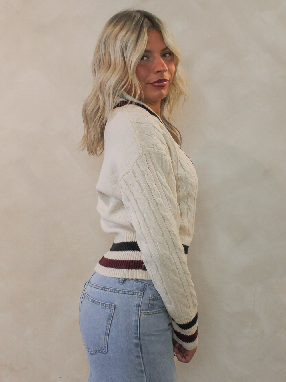Woman wearing a cream colored sweater with varsity stripe details