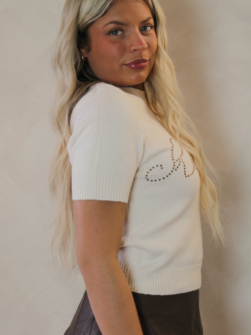 Model wearing a cream sweater with cheers written across the front in rhinestones