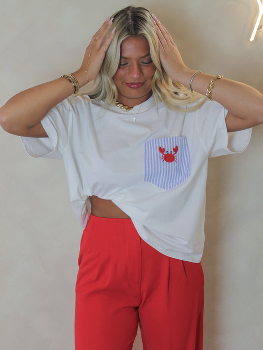 Woman wearing a white oversized shirt with a striped pocket design with an embroidered crab, paired with red pants