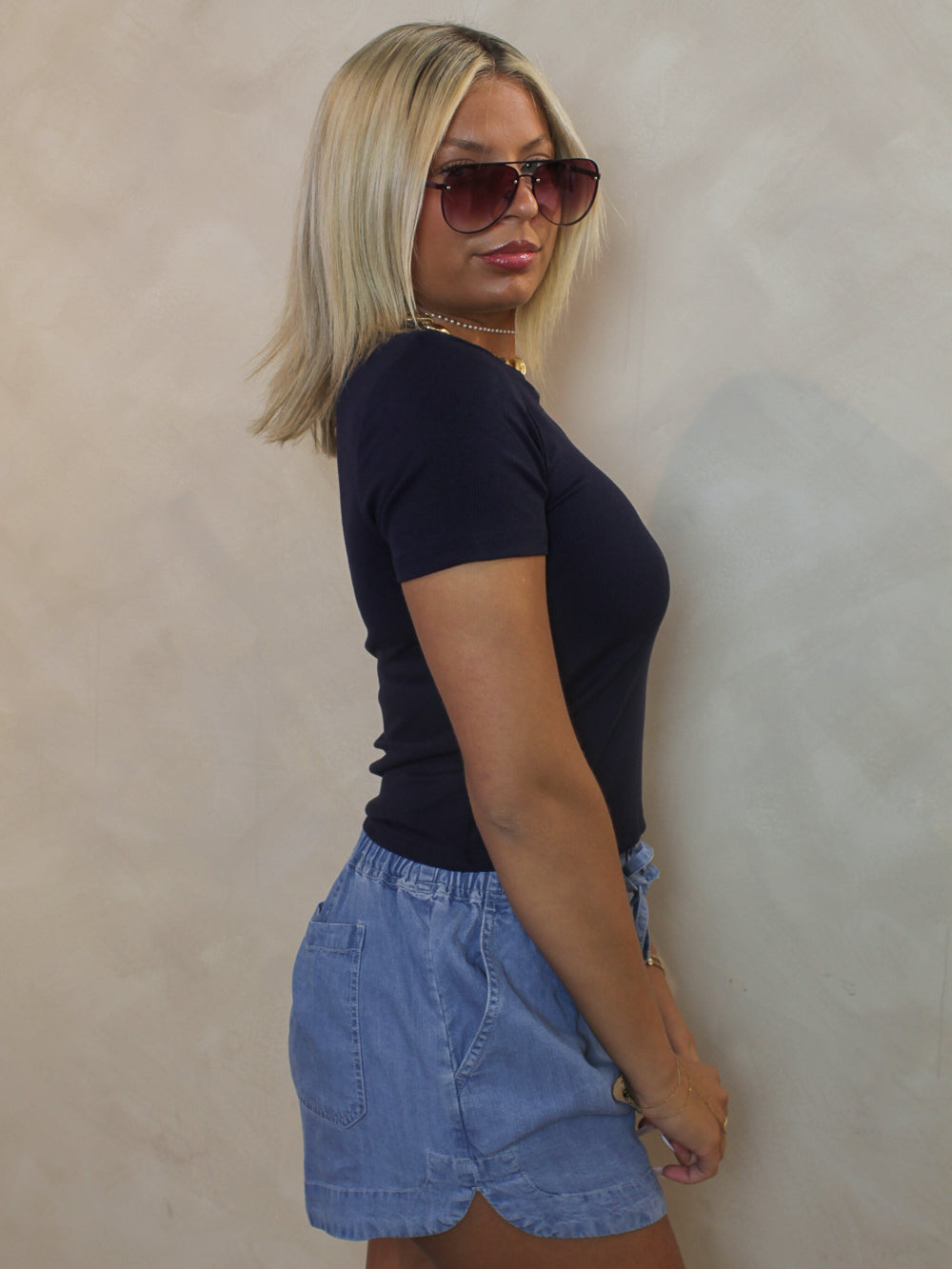 Woman wearing a navy blue tee shirt with denim shorts and red sunglasses. A fourth of july outfit