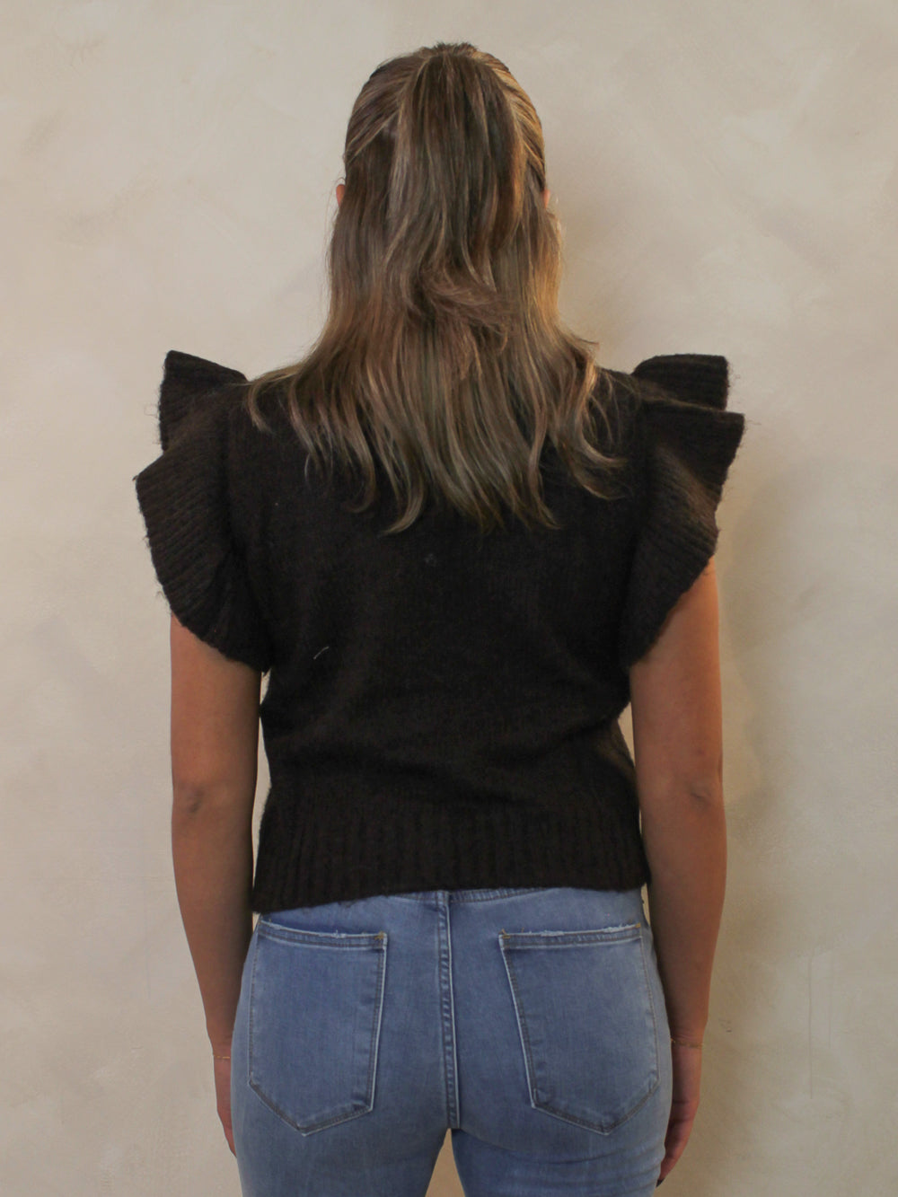 Back view of a dark brown ribbed sweater with a mock neck and dramatic ruffle cap sleeves.