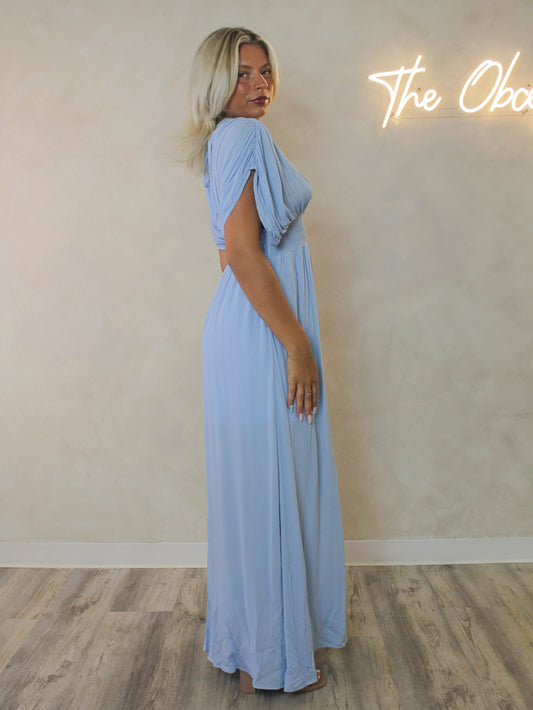 A woman modeling a light blue maxi dress with draped short sleeves.