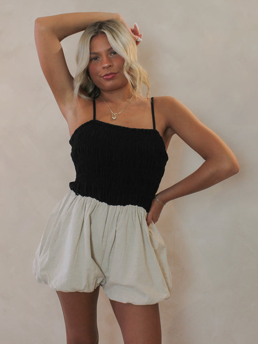 Woman wearing a two-tone romper with a black smocked top and light balloon shorts