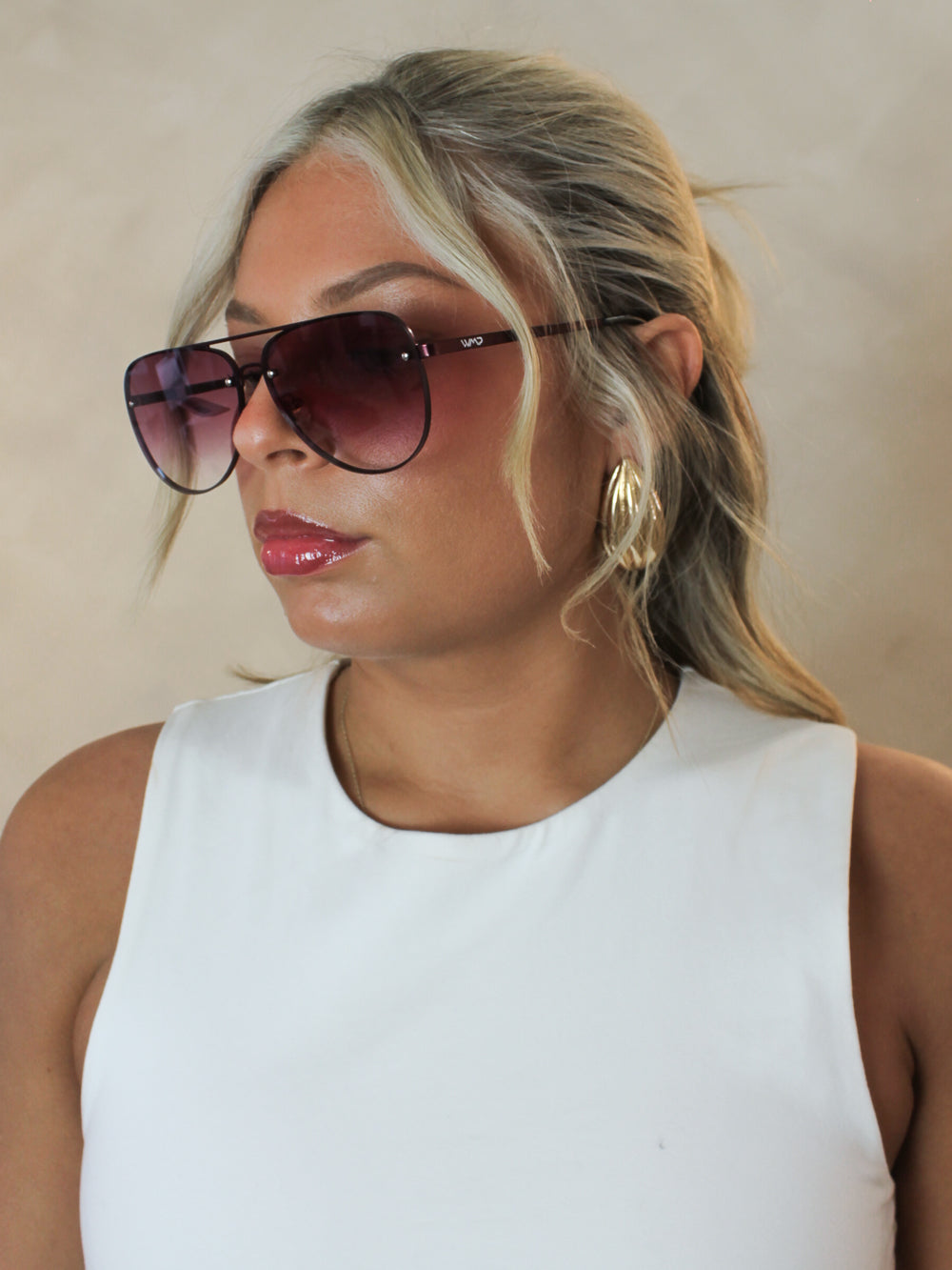 Woman wearing oversized aviator sunglasses with a rimless look, gradient burgundy lenses and matching metal frame.