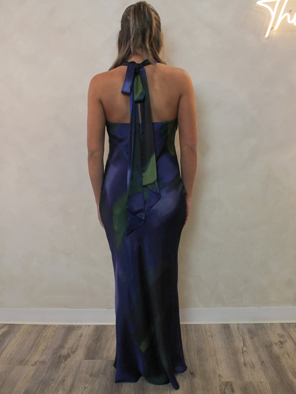 Back view of  a navy satin maxi dress with a tie halter neckline.