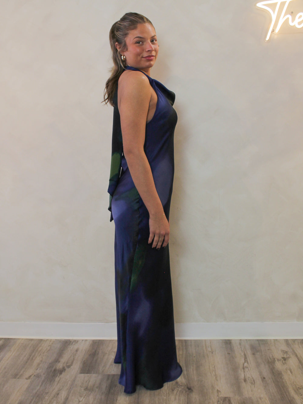 Side view of a navy floor length dress with a cowl neck and haltert tie.