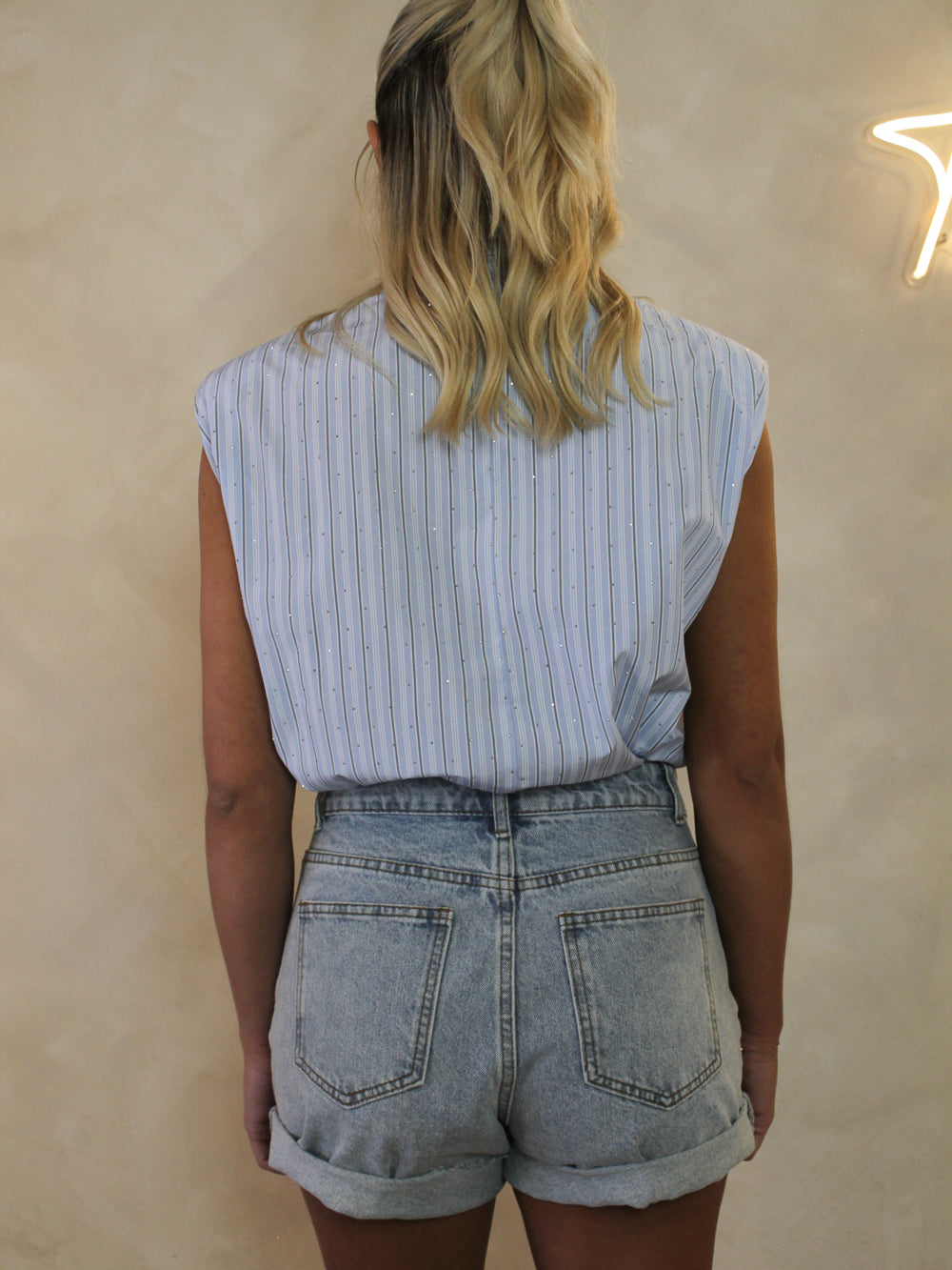 Back view of a woman wearing a light blue, sleeveless pinstripe top with diamente stones all over