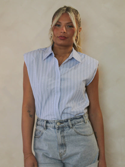 Woman wearing a light blue, sleeveless pinstripe top with diamente stones all over