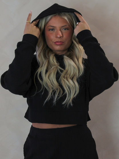 Model wearing a black ribbed long sleeve top with a hood