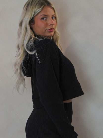 Model wearing a black cropped, long sleeve top with hood