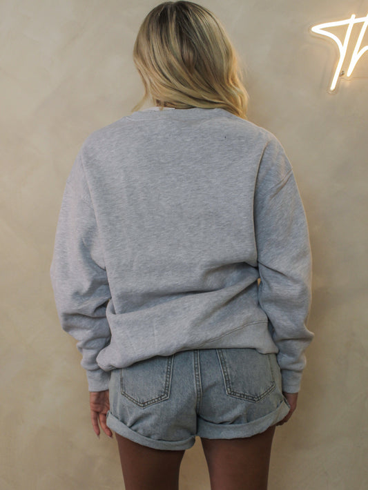 A woman viewed from behind wearing a light heather gray crewneck sweatshirt and light-wash denim short.