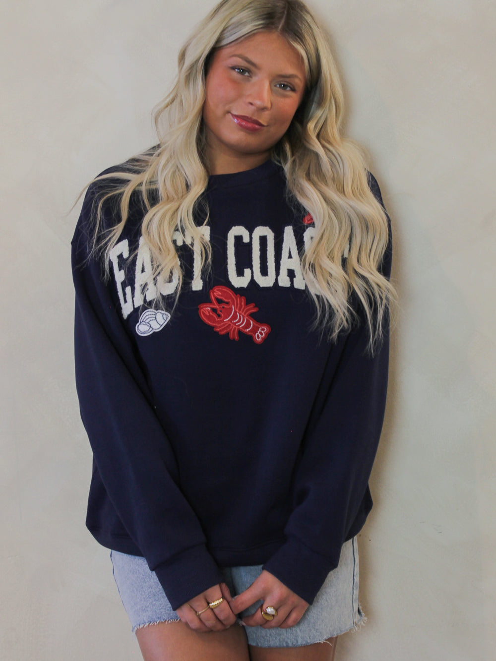 Model wearing a navy blue sweatshirt with the word East Coast and coastal motifs