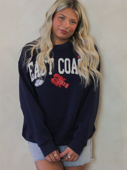 Model wearing a navy blue sweatshirt with the word East Coast and coastal motifs