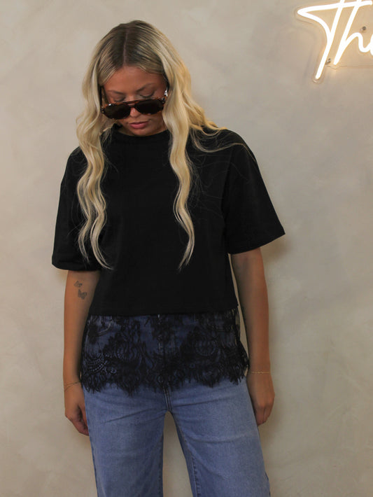 Model wearing a black tee shirt with a thick lace hem styled with sunglasses and flare denim