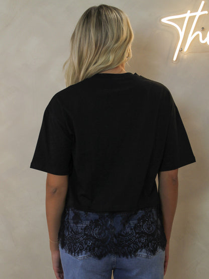 Back view of a black woman's t-shirt with a contrast lace hem. 