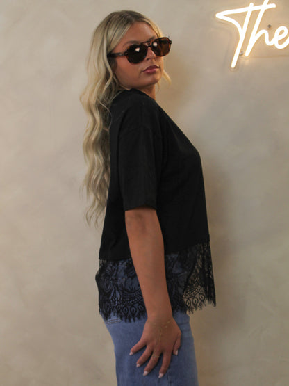 Side view of a model wearing denim and a black oversize t-shirt with a black lace trimmed hem