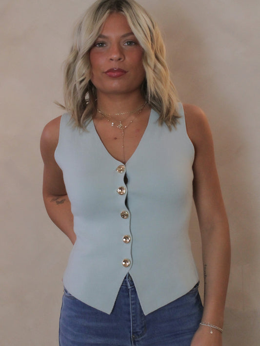 Woman wearing a light blue sleeveless vest with gold buttons