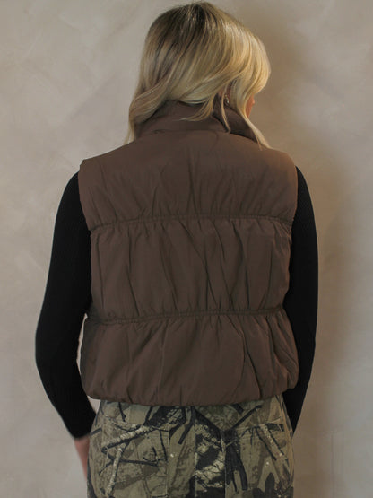 Back view of a woman wearing a brown cropped puffer vest 