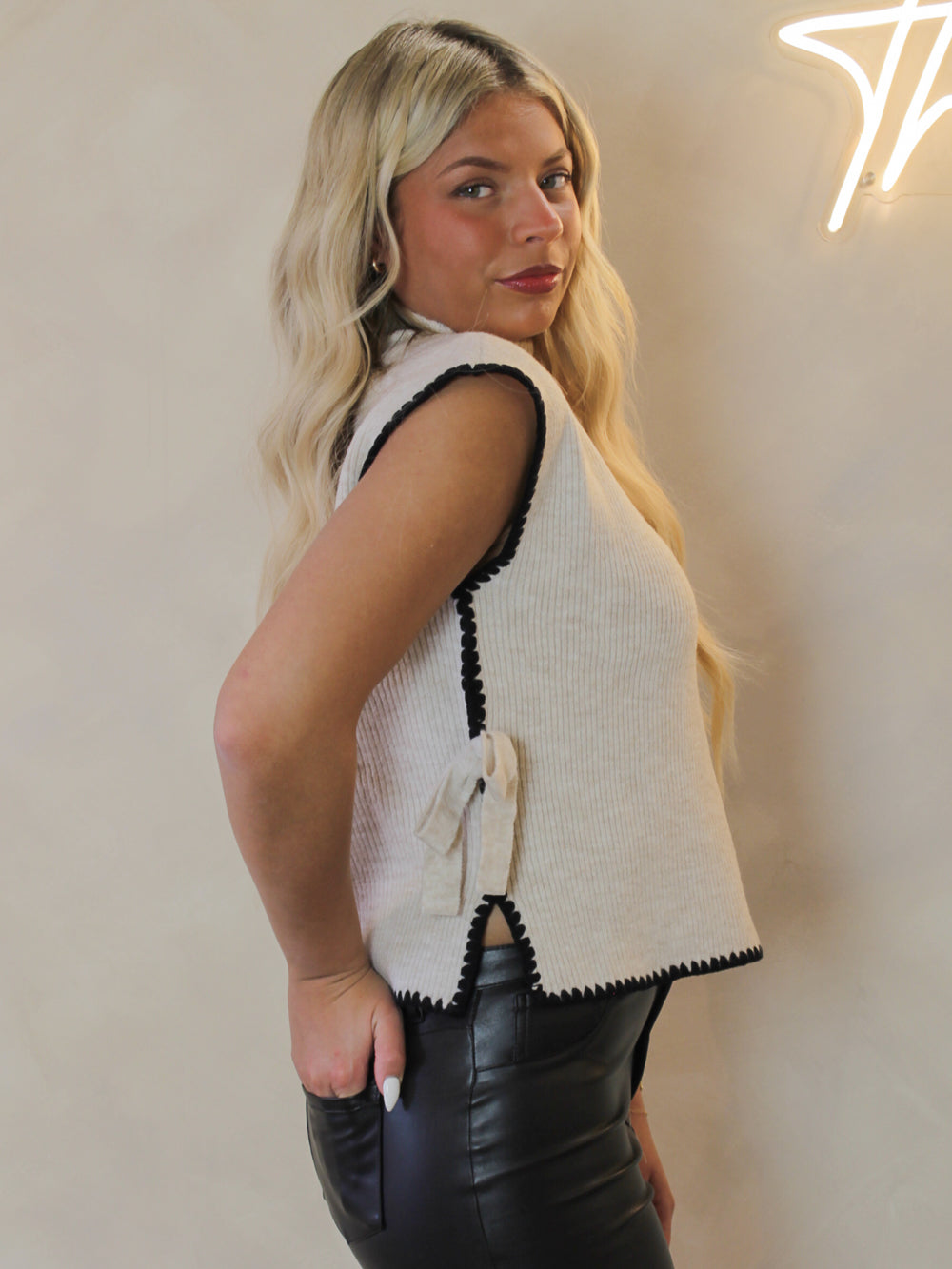 Woman wearing a cream sleeveless sewater with black trim and bow accents 