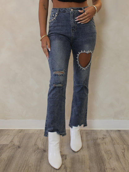 Woman wearing a pair of cropped, medium wash denim with cut out heart and rhinestone details 